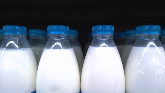 Raw of Milk in plastic bottles with blue caps on black background. Dairy shop. Supermarket. Food and Retail industry. Natural farmer products without fat substitute. Grocery shopping.