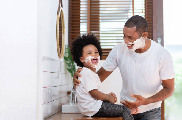 African American Man and little boy having fun laughing with shaving foam on their faces in bathroom at home. Funny Happy Black Father and son shaving faces in the morning African American Man and little boy having fun laughing with shaving foam on their faces in bathroom at home. Funny Happy Black Father and son shaving faces in the morning together. shaving stock pictures, royalty-free photos & images