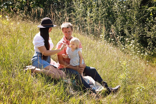 A family with a baby girl, sixteen months old, blow bubbles as they sit on a quilt in a meadow on a summer day.