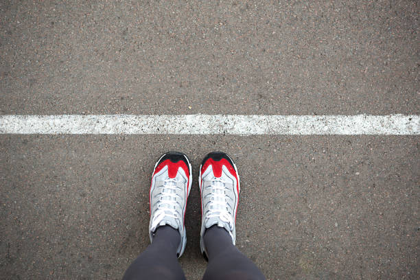 i piedini delle sneakers si trovano vicino alla linea di demarcazione sull'asfalto. linea di delimitazione, distanza sociale, attesa in fila. il bordo, mettiti in fila per cominciare. spazio di copia - boundary foto e immagini stock