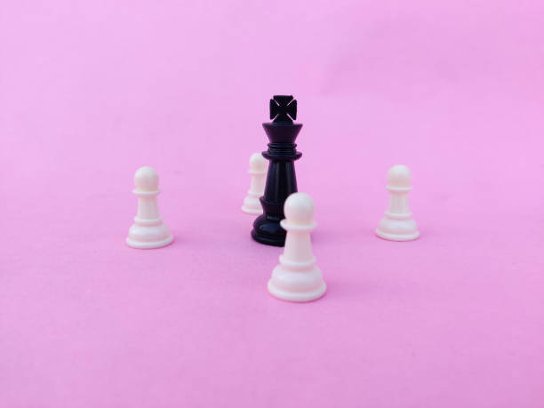 istock Black chess queen surrounded by white chess pawns. Isolated on pink background. 1297795203
