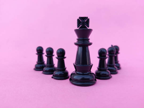 istock Chess leadership concept. Black chess king with black chess pawns. Isolated on pink background. 1297795238