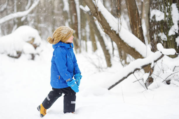 istock Little boy having fun playing with fresh snow in forest. Active outdoors leisure for child in snowy winter day. 1297796874