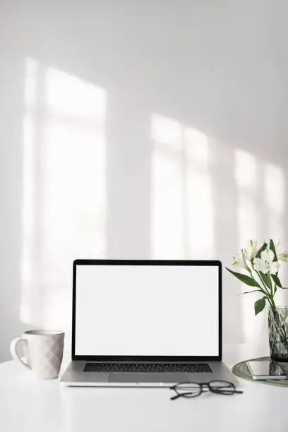 Photo of Place of work. Laptop with blank empty screen, coffee, headset, glasses at home desk