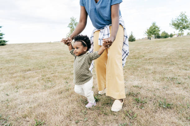 istock Mom helping her toddler walk in a field 1297798329