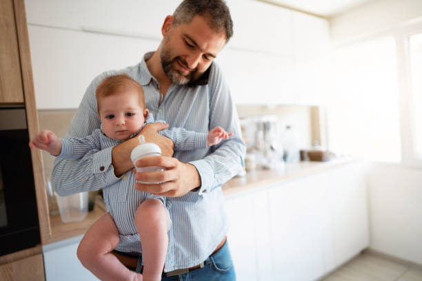 istock Caucasian ethnicity man holding his baby boy while on phone working from home 1297800755
