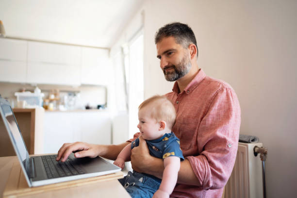 istock Man holding his son and working on laptop from home 1297800826