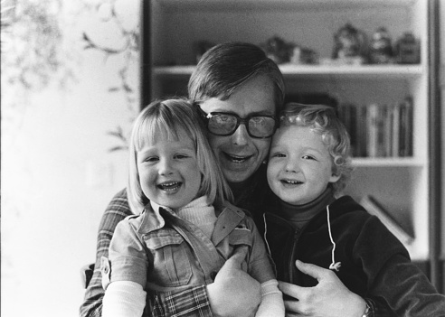 Vintage monochrome 1977 portrait of a happy father making funny faces with son and daughter.