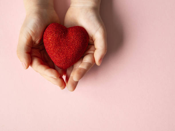 istock Children's hands are holding a red heart on pink background 1297800958