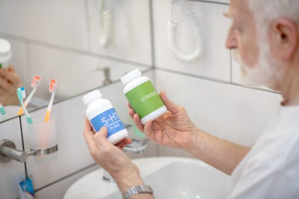 istock Gray-haired man in white tshirt holding bottles with pills and looking thoughtful 1297812100