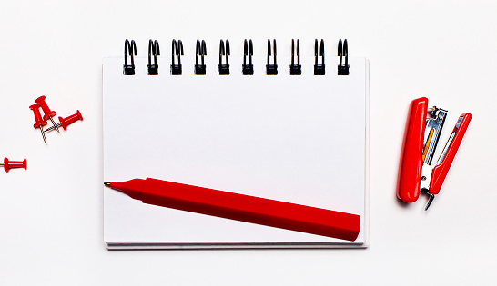 Red pen, stapler and buttons, blank notepad with copy space on a light background. View from above