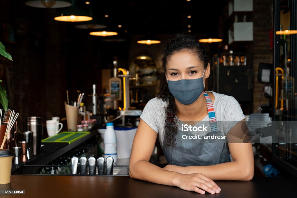 Barista working at a coffee shop wearing a facemask Portrait of a barista working at a coffee shop wearing a facemask during the COVID-19 pandemic and waiting for clients Barista Stock Photo