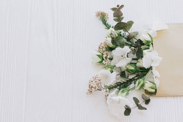 istock Roses, hydrangea, and eucalyptus branches growing from craft envelope on white wood, copy space 1297816759