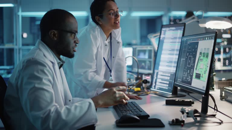 Electronics Research, Development Facility: Engineer Project Manager Talks With Scientist working on Computer. Diverse Team of Professionals Design Silicon Microchip, Semiconductors, Motherboard