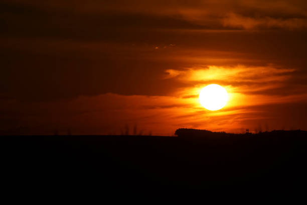 istock Dramatic sunset at sunset, the sky is orange and red with dramatic dark clouds. A silhouette of a silo can be seen on the horizon before the sun. Europe Hungary 1297823420