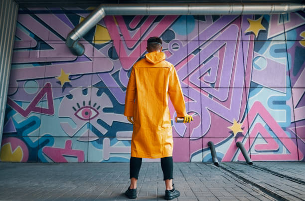 Back view of graffiti painter looking to the wall with his paintings