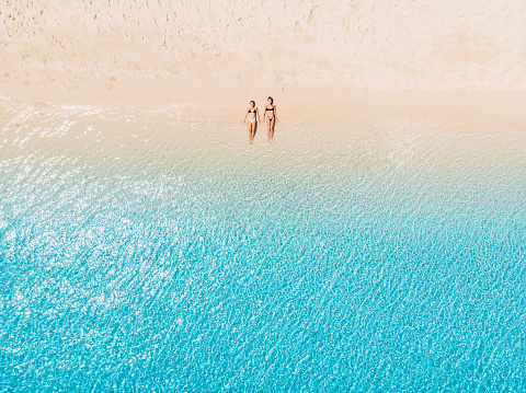 Couple of woman relaxing at paradise beach with blue sea. Aerial view