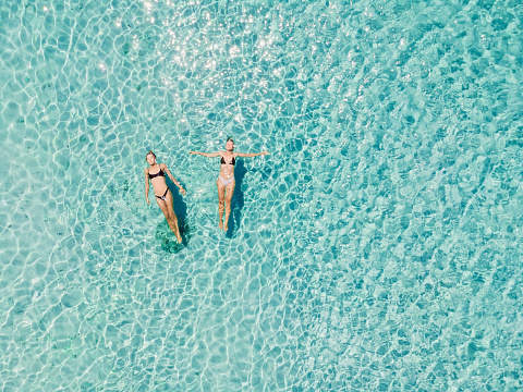 Couple of woman floating in transparent blue ocean. Aerial view