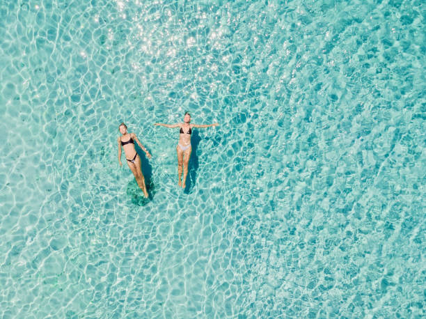 duas mulheres flutuando em oceano azul transparente. vista aérea - seychelles sea lagoon tropical climate - fotografias e filmes do acervo