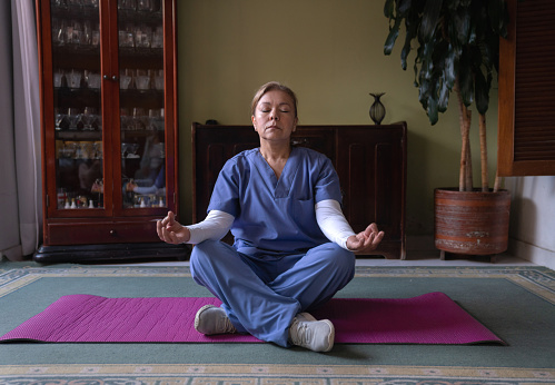 Latin American nurse doing yoga at home after arriving home to relax after a hard day at work - healthcare workers
