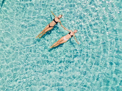Couple of woman floating in clear blue ocean. Aerial view