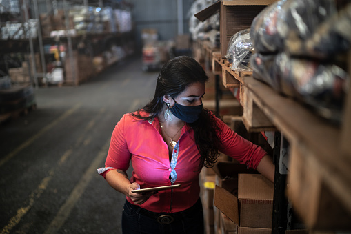 Young woman wearing face mask working in quality control of a distribution warehouse