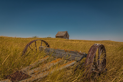 Old wagon with wheels in the long grass with an old wooden farmhouse in the background.