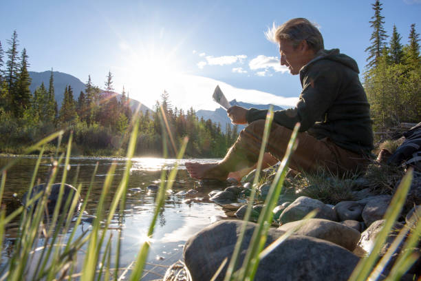 istock Mature man reads map on riverbank at sunrise 1297831506
