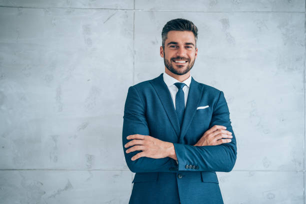 Portrait of a smiling young businessman. Portrait of handsome confident smiling businessman standing with arms crossed in the office and looking at camera. business suit stock pictures, royalty-free photos & images
