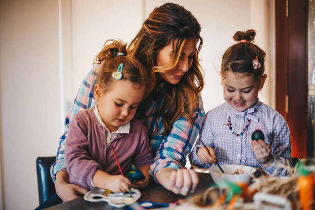 istock Two girls are happy to help their mom in coloring Easter eggs. 1297832989