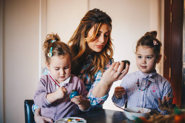 istock Mother is holding her youngest child in lap, while she colors eggs. 1297832992