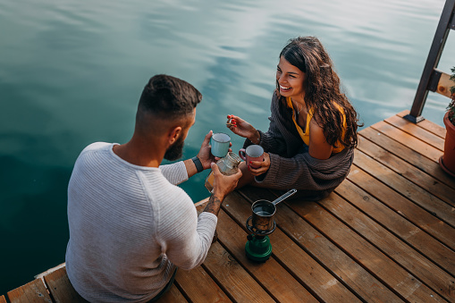 Couple sitting on lake pier and making coffee