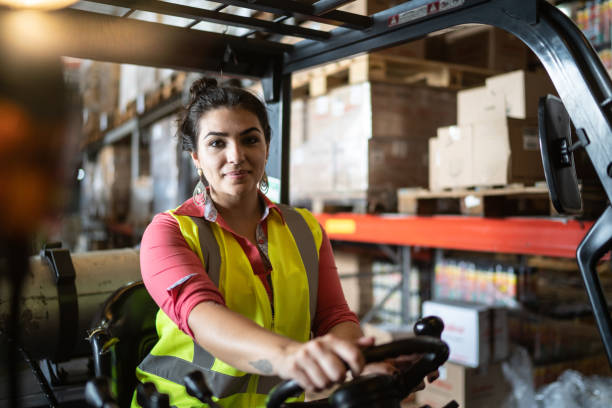 porträt einer jungen frau, die in einer lagerhalle einen gabelstapler fährt - warehouse worker stock-fotos und bilder