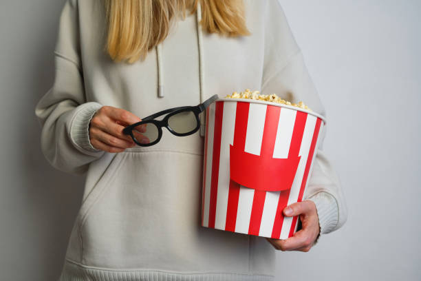 Popcorn paper bucket and 3D glasses in the hands of a young girl preparing to watch a movie. Showtime. Eating delicious unhealthy sweet snacks. Going to cinema for a new film. Rest and entertainment. Popcorn closeup cubo de papel de palomitas de maíz y vasos 3d en manos de una joven que se prepara para ver una película. showtime. comer deliciosos bocadillos dulces poco saludables. ir al cine para una nueva película. descanso y entretenimiento. primer plano de palom