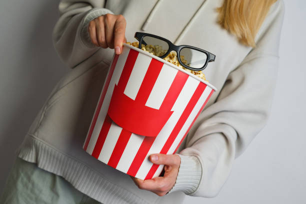 Popcorn paper bucket and 3D glasses in the hands of a young girl preparing to watch a movie. Showtime. Eating delicious unhealthy sweet snacks. Going to cinema for a new film. Rest and entertainment. Popcorn closeup cubo de papel de palomitas de maíz y vasos 3d en manos de una joven que se prepara para ver una película. showtime. comer deliciosos bocadillos dulces poco saludables. ir al cine para una nueva película. descanso y entretenimiento. primer plano de palom
