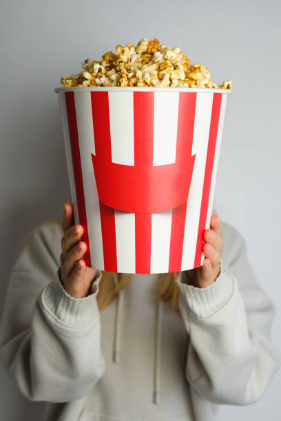 Popcorn paper bucket in the hands of a young girl preparing to watch a movie. Showtime. Eating delicious unhealthy sweet snacks. Going to cinema for a new film. Rest and entertainment. Popcorn closeup cubo de papel de palomitas de maíz en las manos de una joven que se prepara para ver una película. showtime. comer deliciosos bocadillos dulces poco saludables. ir al cine para una nueva película. descanso y entretenimiento. primer plano de palomitas de