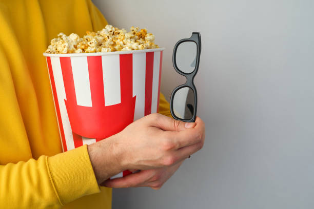 Popcorn paper bucket and 3D glasses in the hands of a men preparing to watch a movie. Showtime. Eating delicious unhealthy sweet snacks. Going to cinema for a new film. Rest and entertainment. Popcorn closeup cubo de papel de palomitas de maíz y vasos 3d en manos de un hombre que se prepara para ver una película. showtime. comer deliciosos bocadillos dulces poco saludables. ir al cine para una nueva película. descanso y entretenimiento. primer plano de palom