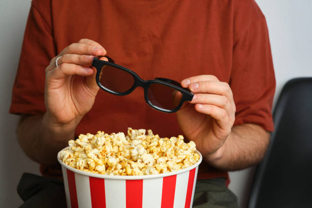 Popcorn paper bucket and 3D glasses in the hands of a men preparing to watch a movie. Showtime. Eating delicious unhealthy sweet snacks. Going to cinema for a new film. Rest and entertainment. Popcorn closeup cubo de papel de palomitas de maíz y vasos 3d en manos de un hombre que se prepara para ver una película. showtime. comer deliciosos bocadillos dulces poco saludables. ir al cine para una nueva película. descanso y entretenimiento. primer plano de palom