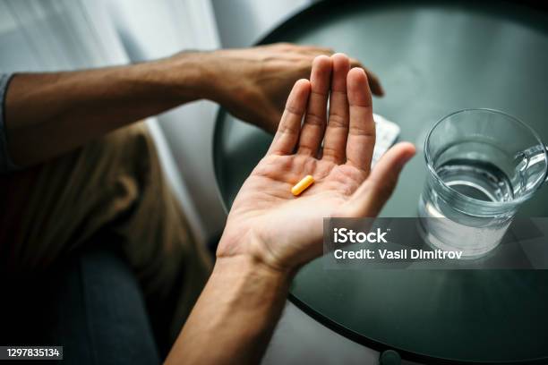 Unrecognizable Man Holding A Pill In Front Of A Table With Glass Of Water Medical Treatment Drug Use Concept Stock Photo - Download Image Now