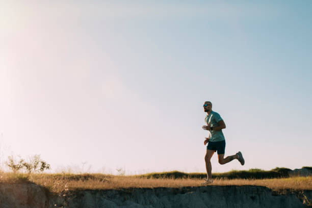 Active Lifestyle: Man in Blue Sportswear Running on a Dirt Road in the Countryside Fit runner during his morning workout (wide angle, copy space) hot handsome man stock pictures, royalty-free photos & images