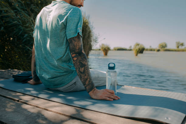 istock Anonymous Man Sitting on a River Bank and Doing Yoga 1297835625