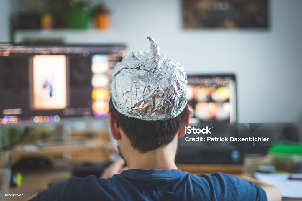 Conspiracy theory concept: young man is wearing aluminum head, sitting in front of the pc watching videos Young man is wearing aluminum cap, conspiracy theory concept Conspiracy Theory Stock Photo