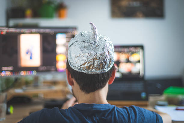 Conspiracy theory concept: young man is wearing aluminum head, sitting in front of the pc watching videos Young man is wearing aluminum cap, conspiracy theory concept stupid computer i hate you stock pictures, royalty-free photos & images
