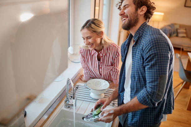 encantadora pareja haciendo los platos juntos - lavar los platos fotografías e imágenes de stock