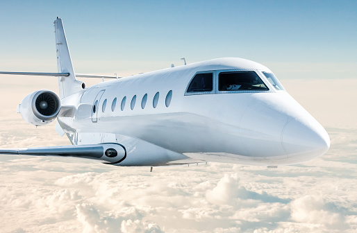 White modern luxury business jet flies in the air above the clouds. Close-up view corporate airplane