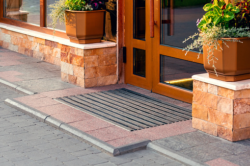 threshold with a foot mat at the front door with a stone facade and flowerpots, closeup architecture.