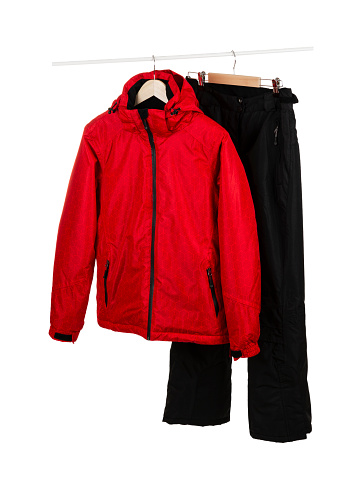 Red ski waterproof and windproof jacket and black pants on hangers isolated on white background.