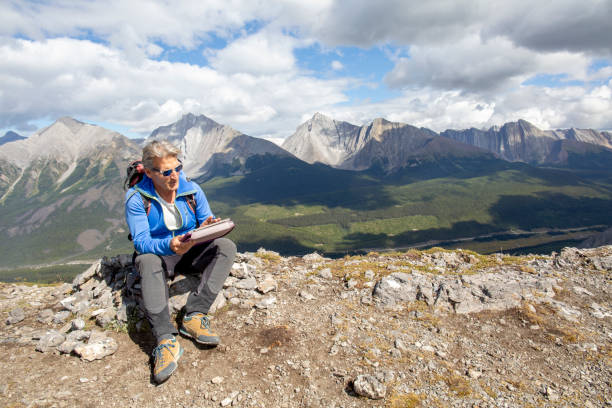 Male mountaineer reaches mountain summit He looks at digital tablet, plans route ahead environment computer cloud leadership stock pictures, royalty-free photos & images