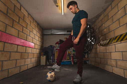Young caucasian man playing with a soccer ball at the garage