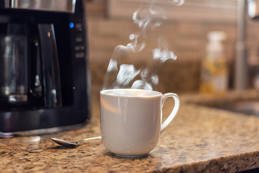 Steaming cup of hot coffee on the kitchen counter in morning sunlight